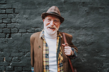 Waist up portrait of joyful hipster pensioner posing near black wall outdoor and happy smiling