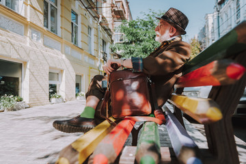 Full length side portrait of good looking thoughtful senior male resting on colorful bench outdoor