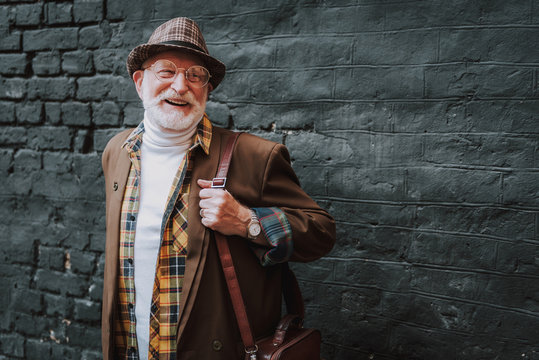 Waist up portrait of joyful hipster pensioner standing near black wall and smiling. Copy space on right side