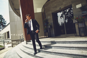 Cheerful confident elegant man smiling and walking downstairs while talking on the phone