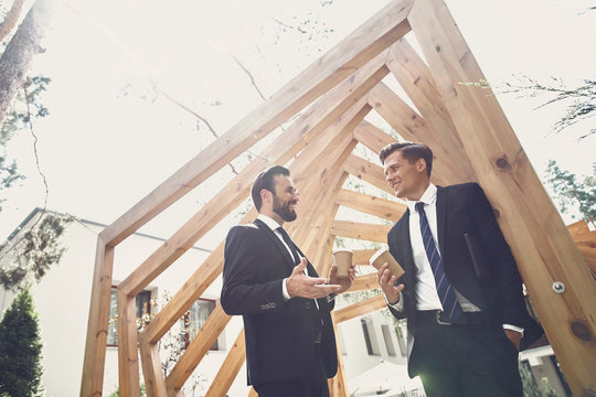 Relaxed young men having free time and smiling while drinking coffee outdoors