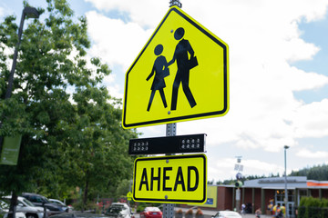 School zone crossing sign with pedestrians and word 'ahead'.