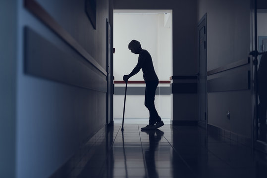 Lady is standing in hospital corridor. She is using cane for walking. Copy space in left side