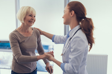 Focus on smiling mature lady with crutch while she is thanking and saying good bye to female physician. They are standing together in medical office and kindly hand-holding