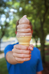 Boy holding a melting soft serve ice cream cone in the summertime covering his face