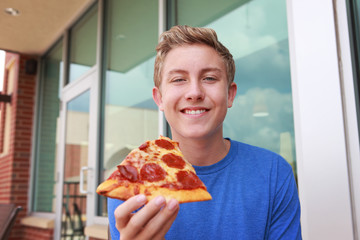 Image of a smiling boy holding a piece of pepperoni pizza © soupstock