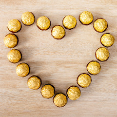 Fototapeta na wymiar Chocolate balls in foil arrange in Heart Shape on wood background