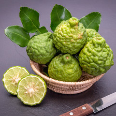 Fototapeta premium Bergamot, kaffir lime and kaffir lime leaf with basket and knife on dark background