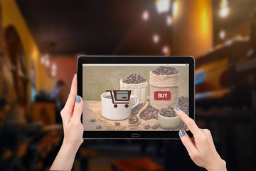 Shopping online concept, Hand using mock up computer tablet, with picture hot cup of coffee with beans on burlap sack on coffee shop cafe background, and copy space