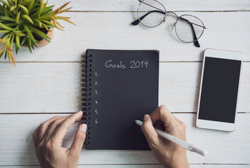 2019 goals text on notebook with smartphone on white wooden desk, Top view © Kittiphan