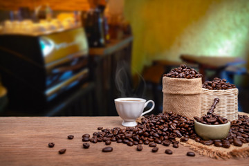 Hot cup of coffee  and beans with burlap sack on the wooden table, with coffee shop background. copy space