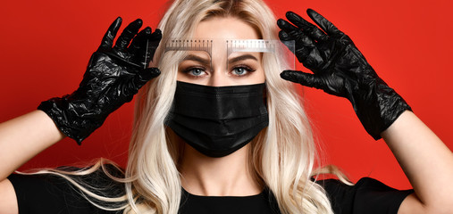 Beautician doing tattooing eyebrow permanent make-up for eyebrows in black gloves and mask on red background - obrazy, fototapety, plakaty