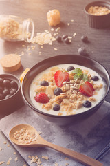 bowl of oat granola with yogurt, fresh strawberry, blueberries and nuts on black wooden table