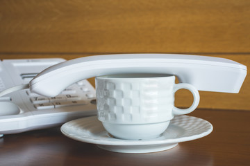 Tube from office phone on white cup with saucer for coffee.