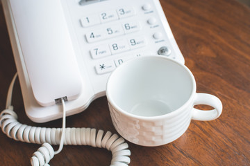 Office phone with empty cup for coffee on wooden table.