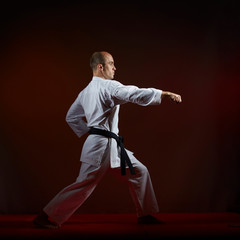 On a dark background, an athlete with a black belt trains formal karate exercises
