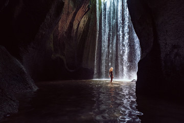 Woman stand in underground cave pool under falling fresh water of Tukad Cepung waterfall. Nature...