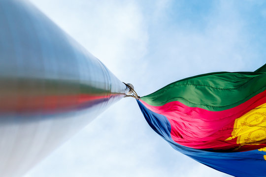 The flag of the Krasnodar Territory is developing in the wind. A massive flagpole with a reflection of the flag