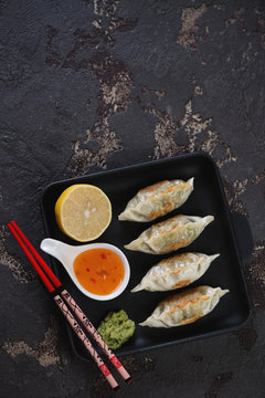 Cast-iron serving tray with pan fried korean dumplings. Flatlay with copyspace on a dark brown stone background, vertical shot