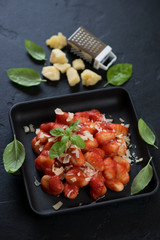 Potato gnocchi with strained tomatoes and grated parmesan in a cast-iron serving pan, studio shot on a black stone background