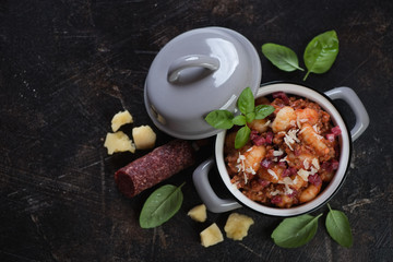 Potato gnocchi with minced meat, slices of salami, grated parmesan and green basil. Top view on a dark brown stone background with space