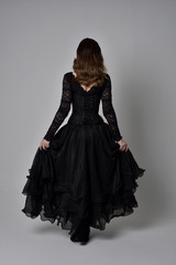 full length portrait of brunette girl wearing long black lace gown with corset.  standing pose with...
