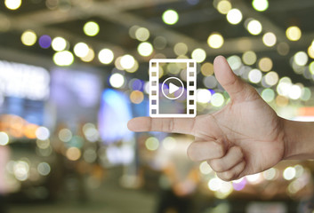 Play button with movie icon on finger over blur light and shadow of shopping mall, Business cinema online concept
