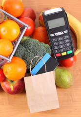 Payment terminal, contactless credit card and paper shopping bag with fruits and vegetables