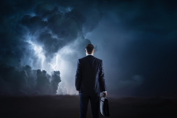 Trouble ahead, businessman standing in front of a stormy sky