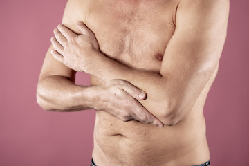 The man holds the elbow due to acute pain. Isolated on a pink background