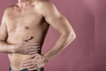 Fototapeta na wymiar Man suffering from pain in his side. Pink background. Stomach pain, pancreas, kidneys