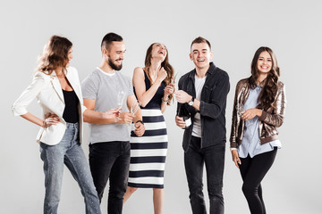 Obraz premium Company of friends in fashionable casual clothes stand together and smile. Guy opens a bottle of champagne