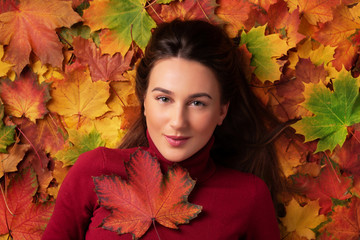 Naklejka na ściany i meble Girl holding red maple leaf in hand over colorful fallen leaves background. Top view. Copy space for advertising. Sunny day, warm weather. Gold cozy autumn concept