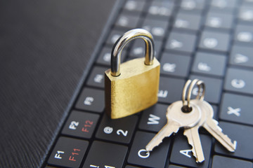 Golden locked padlock and keys on black computer laptop or tablet keyboard. Concept of internet password security, data privacy, cybercrime prevention. Selective focus.