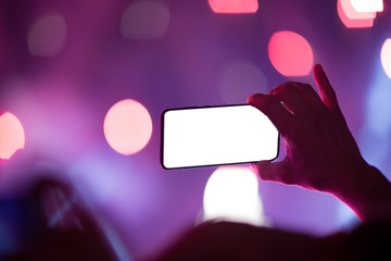 Concert bokeh background, one hand holding the smart phone. Smartphone with white display. 