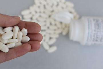 Hand holding many white medicine pills on blurred tablets and pills bottle background.  Pharmacy, healthcare and addiction or committing suicide concept.