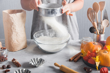 Woman sifts flour using sieve into glass bowl