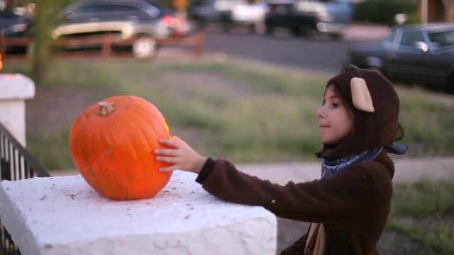 A young girl in a monkey cowgirl costume lovingly admires the pumpkin she carved for Halloween.