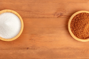 An overhead photo of two bowls of white and brown sugar, shot from above on a dark rustic wooden background with a place for text
