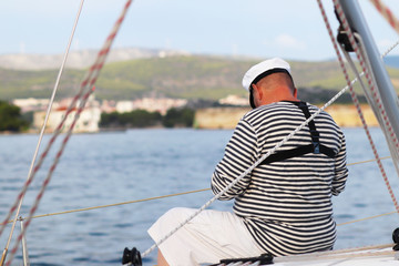 Yachtsman in marine clothing looking into the distance sitting on board a sailing yacht. Sea fishing from the ship. Peaceful state at summer holidays. Travel experienced person around the world.