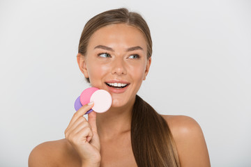 Beauty portrait of brunette shirtless woman with long brown hair smiling and holding colorful cosmetic pads, isolated over white background