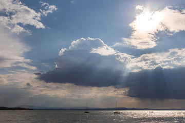 Naklejka na ściany i meble A couple of empty, little sailboat on a lake, beneath a moody sky with sun rays filtering through