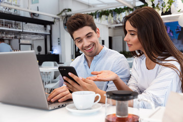 Loving couple sitting in cafe using laptop computer and mobile phone.
