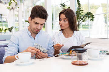 Loving couple sitting in cafe holding check and money.