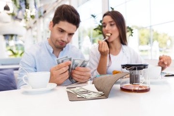 Displeased confused loving couple sitting in cafe holding check and money.