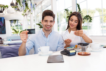 Happy loving couple sitting in cafe holding credit card and check.