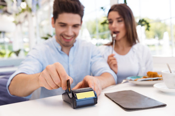Happy loving couple sitting in cafe holding credit card and make payment.