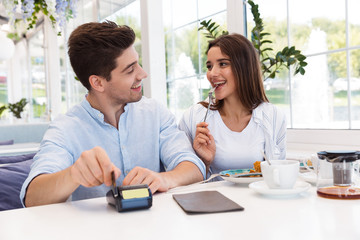 Happy loving couple sitting in cafe holding credit card and make payment.