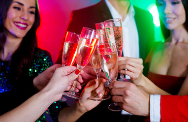 Close view of clinking glasses of sparkling champagne, big company of friends on the christmas or new year perty is celebrating together