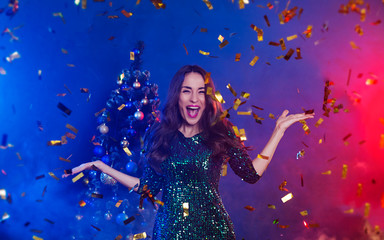 Excited happy and stylish smiling woman posing on colorful christmas tree background and dancing
